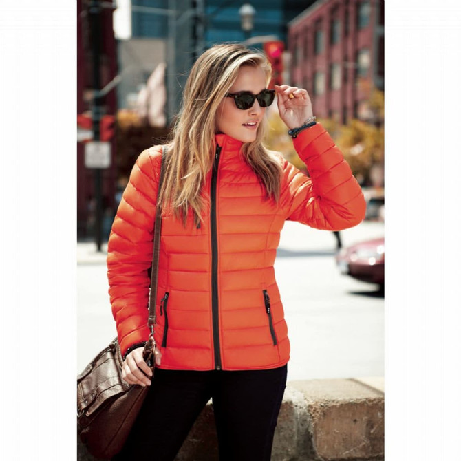 An orange puffer jacket worn by a woman, featuring zippered pockets and a sleek design, set against an urban background.
