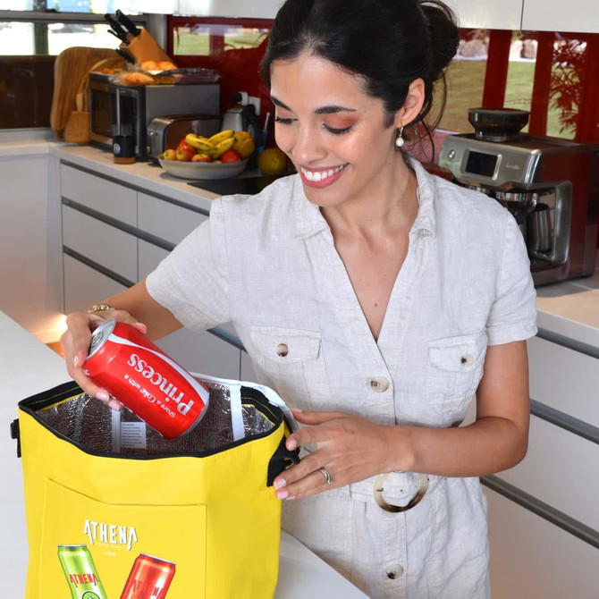 A woman is placing a can inside a bright yellow cooler bag, which features a logo on the front.