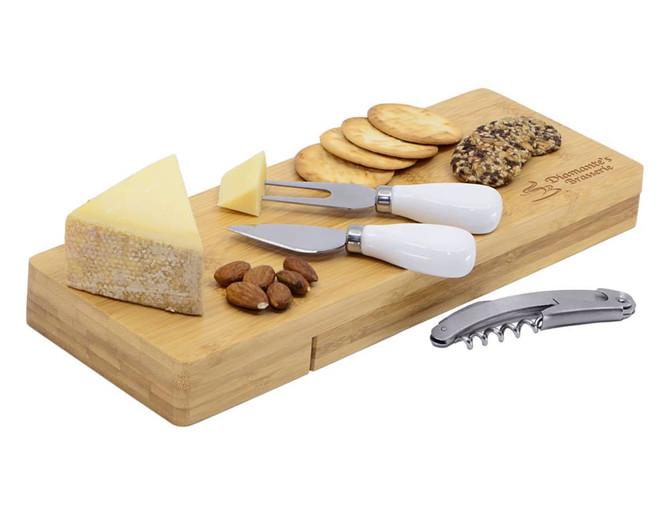 A bamboo cheese board featuring cheese wedges, crackers, almonds, and three cheese knives with white handles.