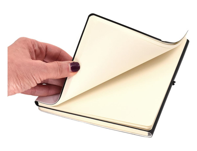 A hand holding an open A5 notebook with blank pages, featuring a black and white cover.