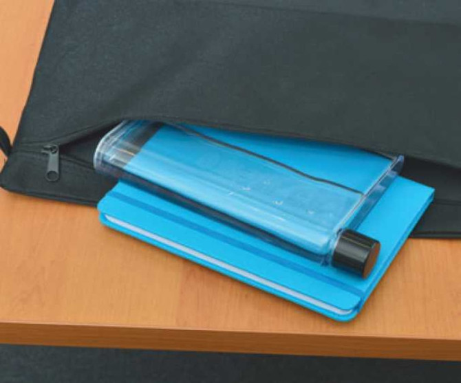 A blue drink bottle with a black lid resting on a blue notepad, placed inside a black bag on a wooden surface.