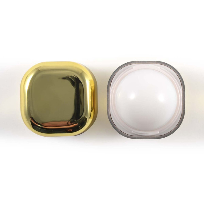 A square cosmetic container with a shiny gold lid and a transparent base, featuring a logo.