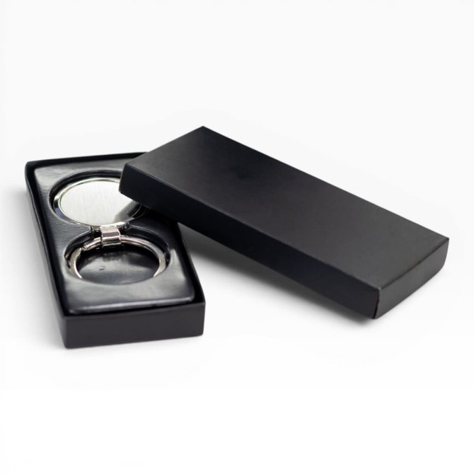 A silver keychain displayed in a black gift box, featuring a sleek design and a glossy finish.