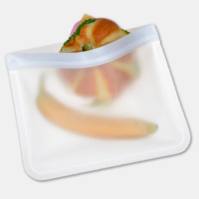 A transparent, reusable PEVA food storage bag containing a sandwich and a banana. Features a zip closure and a logo.