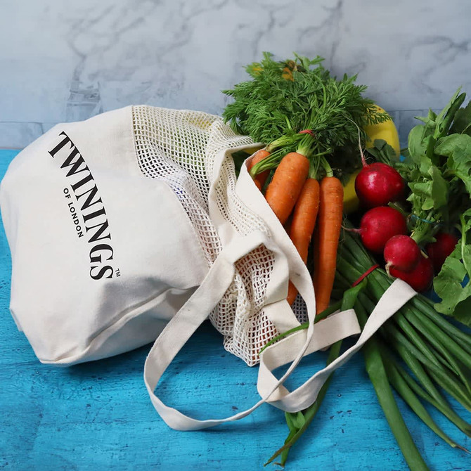 A cotton shopping tote in cream with a mesh top, filled with carrots, radishes, and fresh herbs.