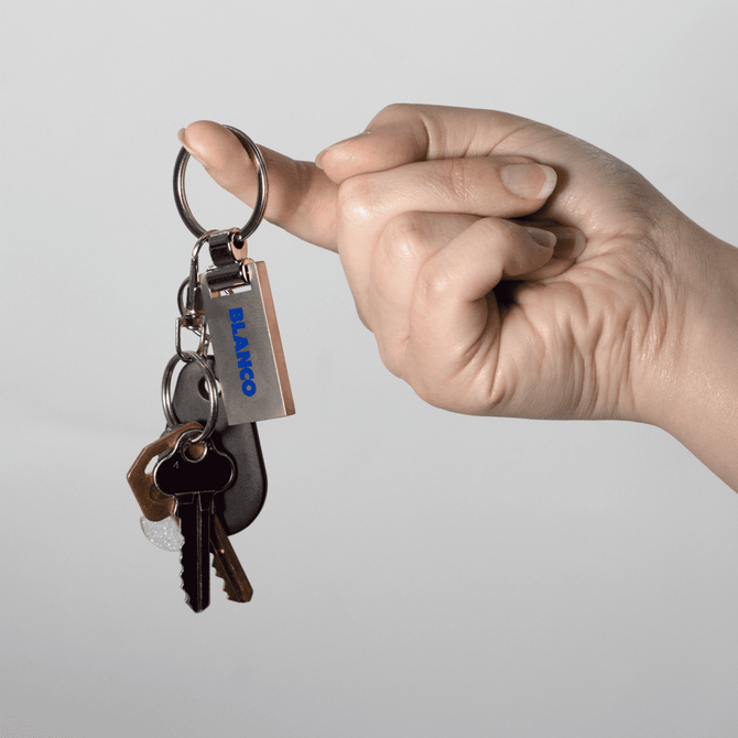 A hand holds a silver keychain attached to several keys, featuring a logo. The overall look is sleek and modern.