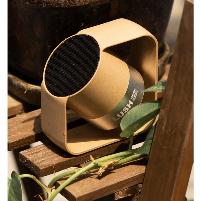 A wireless speaker in a circular design featuring a beige casing and a black speaker grille, set on a wooden surface.
