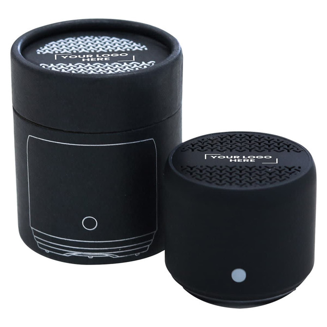 A black Bluetooth speaker with a textured top, placed next to a cylindrical box featuring a logo.