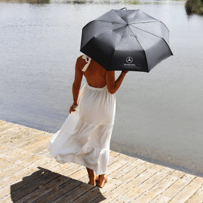 A black umbrella with a logo held by a person in a white dress, standing by the water.