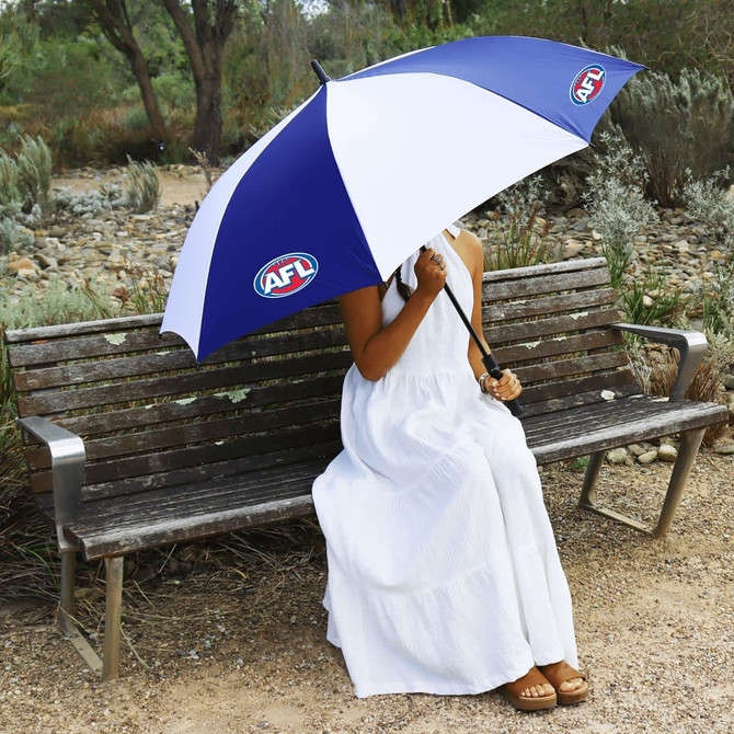 A two-tone blue and white umbrella with a logo, held by a person in a white dress sitting on a bench outdoors.