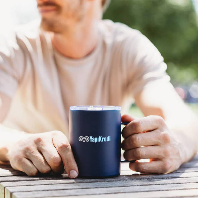 A drink bottle featuring a navy blue mug with a handle, sitting on a wooden table. It has a logo displayed.
