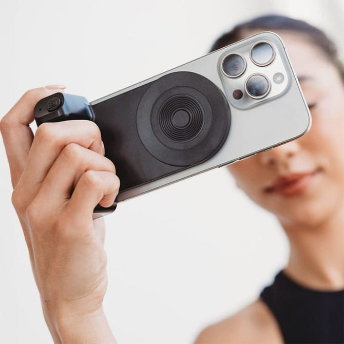 A wireless charger with a circular black design attached to a smartphone, held by a hand.