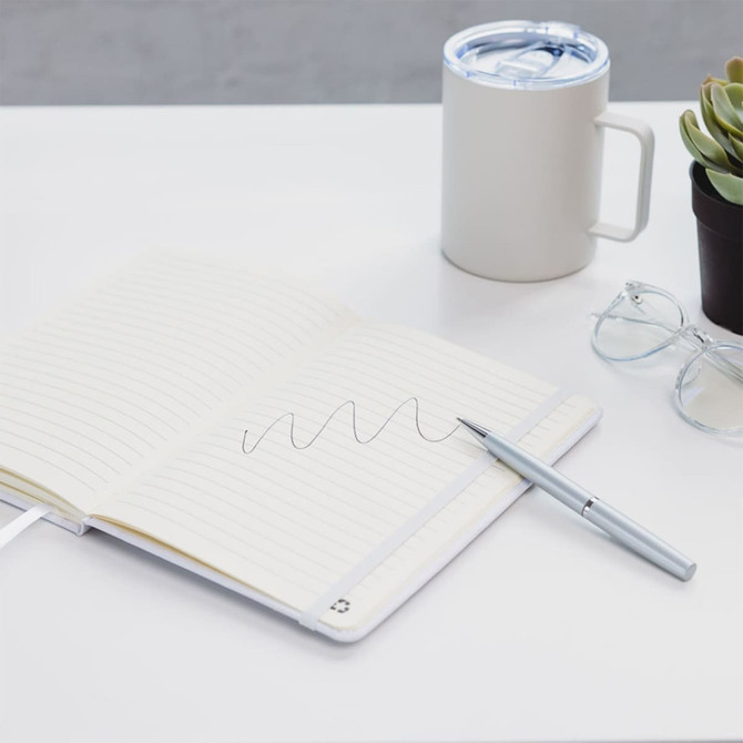 A white A5 notebook with lined pages, a silver pen, a coffee mug, glasses, and a small potted plant on a desk.