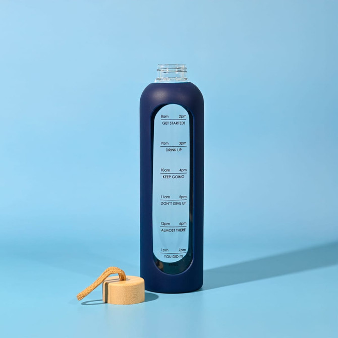 A drink bottle in navy blue glass with a clear portion featuring measurement markings, accompanied by a wooden lid.