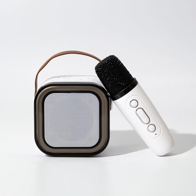 A portable karaoke machine in white and black with a microphone resting beside it. It features a carry handle.