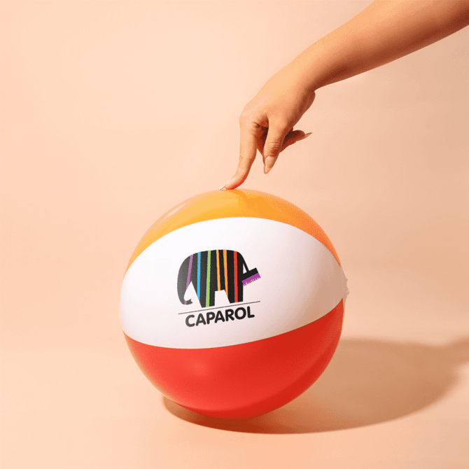 A beach ball in orange, white, and red with a logo, being held by a hand.