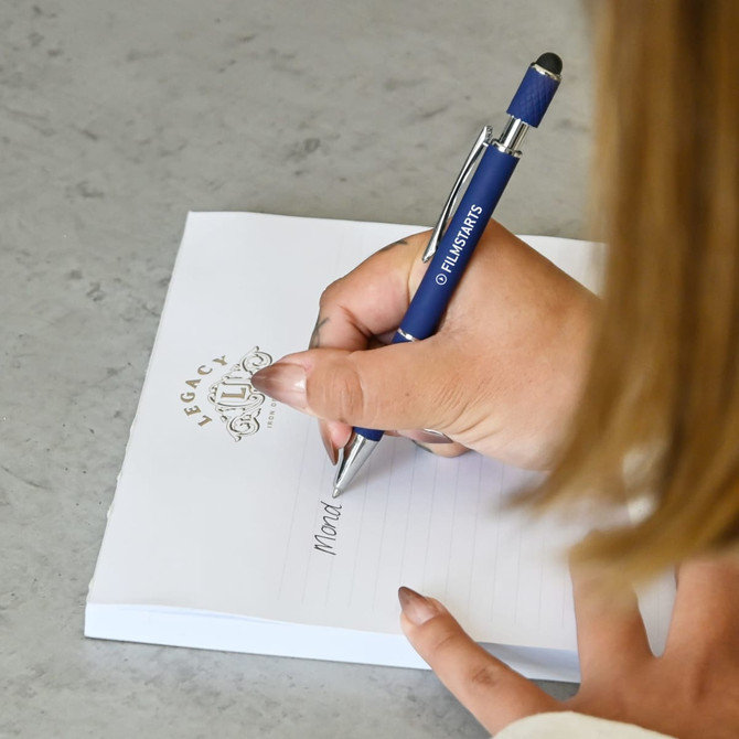 A blue metal pen with a logo is being used to write on a notepad with a decorative header.