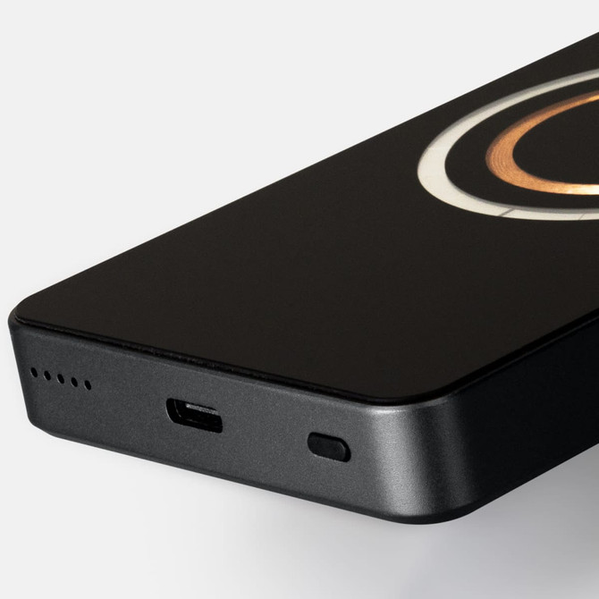 A black wireless charging power bank with a circular design and a USB-C port, featuring a logo.