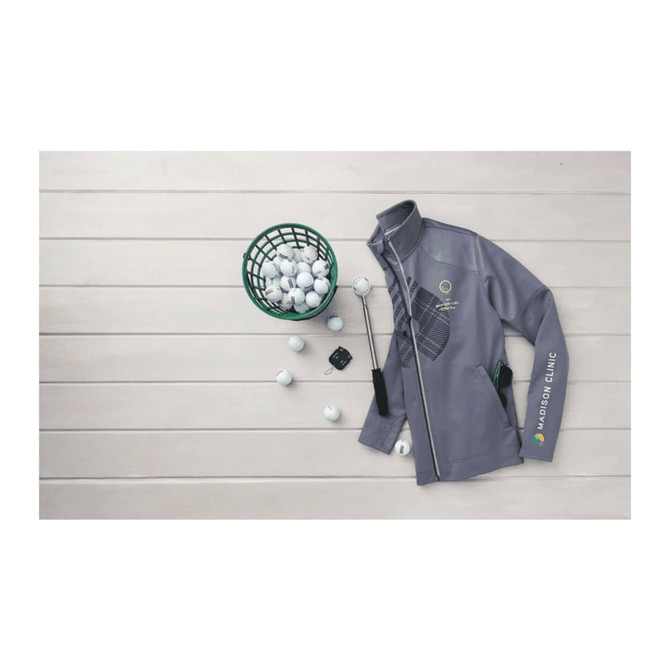 A grey full zip performance jacket with thumb holes and a logo, placed beside a basket of golf balls.