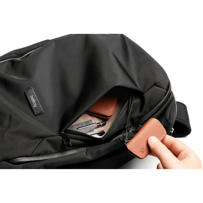 A black backpack features an open pocket with leather tags and various items inside, showcasing its organisational capacity.