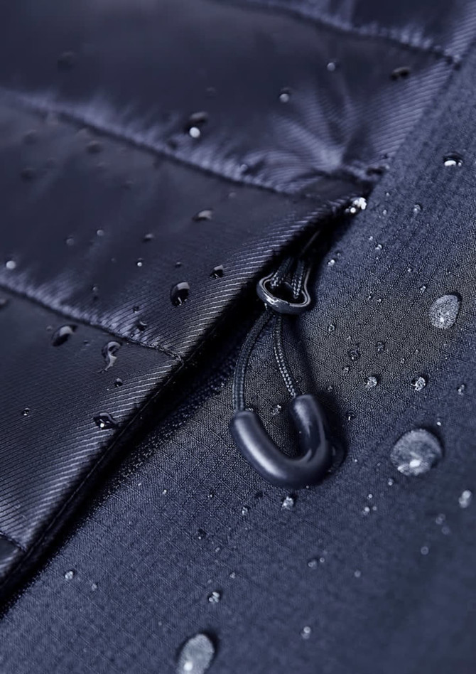 A close-up of a black soft shell jacket featuring a zippered opening and water droplets on the fabric.