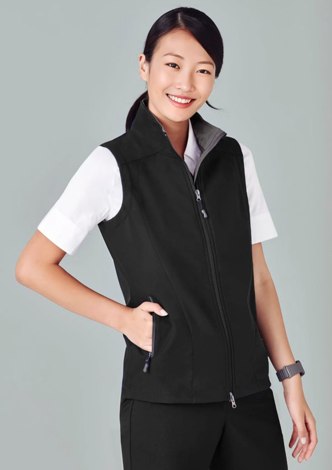 A black women's vest with a zip front, featuring a grey collar and side pockets, worn over a white shirt.