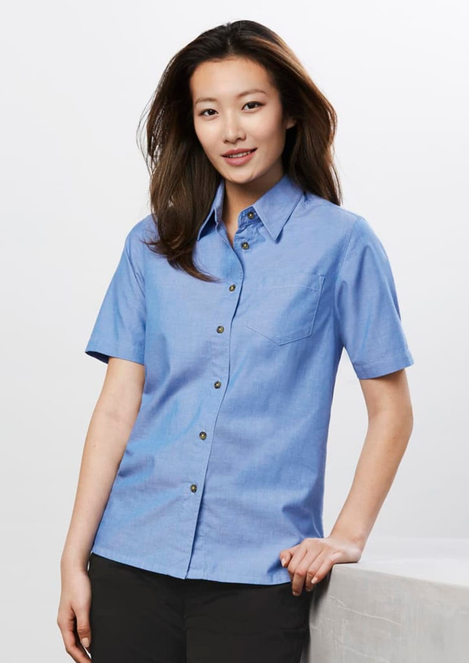 A short sleeve button-up shirt in light blue chambray fabric, featuring a chest pocket and a branded logo.