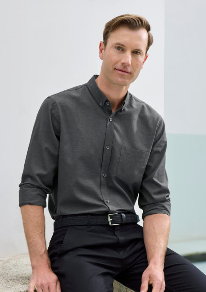 A long sleeve button-up shirt in charcoal grey, featuring a pocket and a branded logo, modelled by a man.