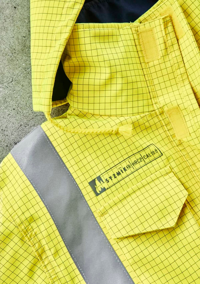 A close-up of a yellow jacket featuring a grid pattern and reflective strips, plus a logo on the front.