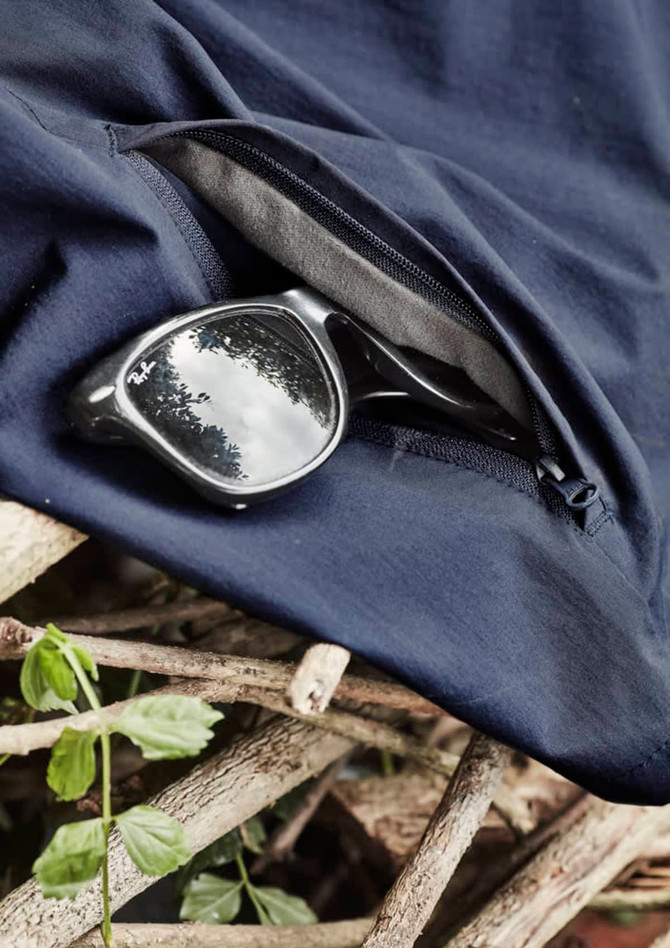 A pair of black sunglasses rests on navy lightweight shorts with a zippered pocket, placed on a textured surface.