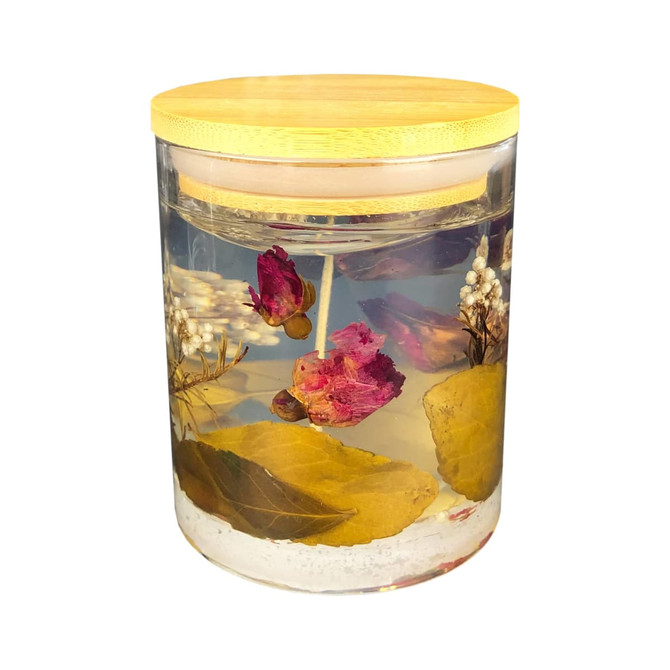 A floral candle in a clear jar featuring dried flowers and leaves, topped with a bamboo lid.