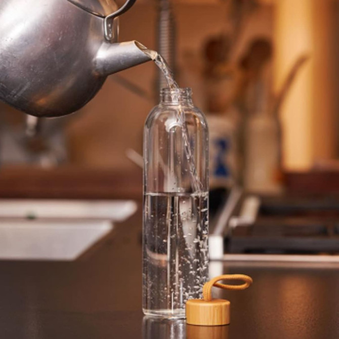 A drink bottle in clear glass with a wooden lid, filled with water, set on a kitchen countertop.