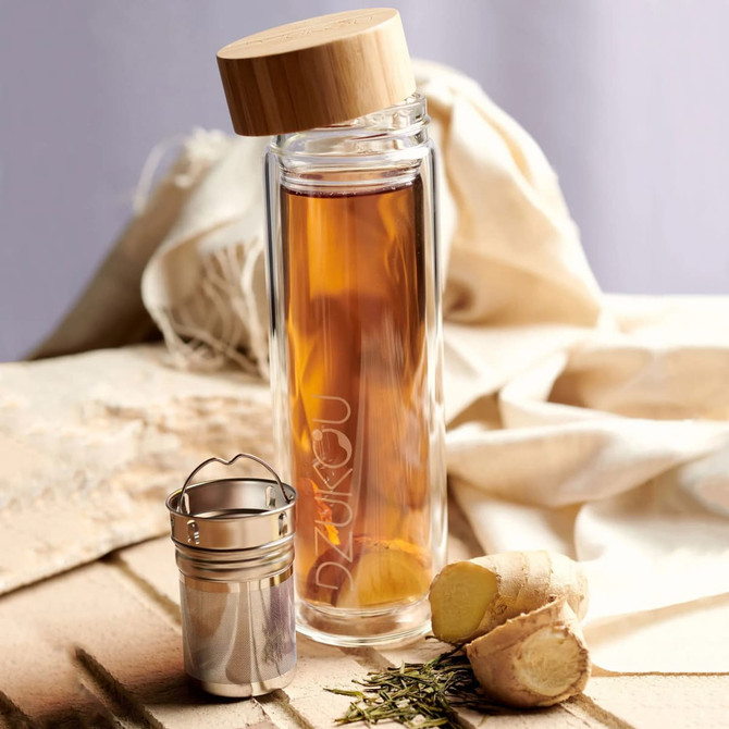 A glass drink bottle with a bamboo lid, containing brewed tea and accompanied by fresh ginger and a tea infuser.
