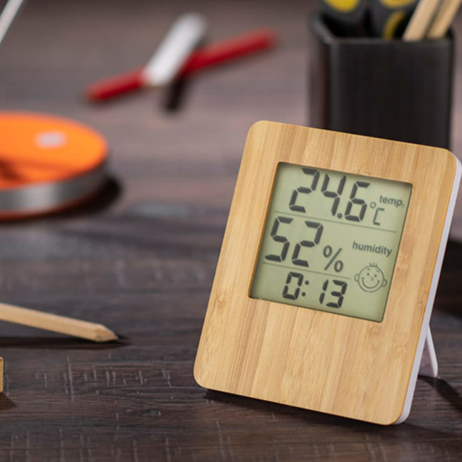 A bamboo desk clock with a digital display showing temperature, humidity, and time, set on a wooden surface.