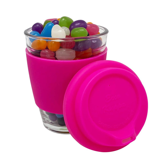 A clear glass coffee cup with a pink silicone sleeve, filled with colourful jelly beans.