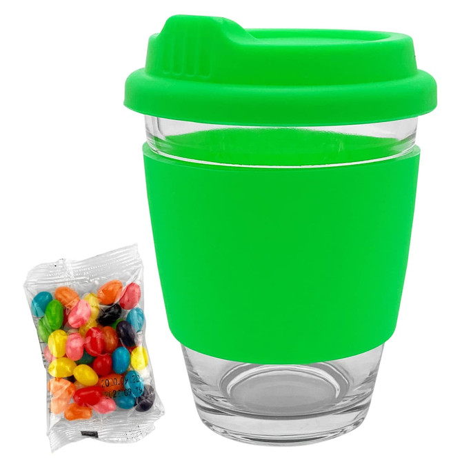 A clear glass coffee cup with a bright green silicone lid and sleeve, alongside a pack of colourful jelly beans.