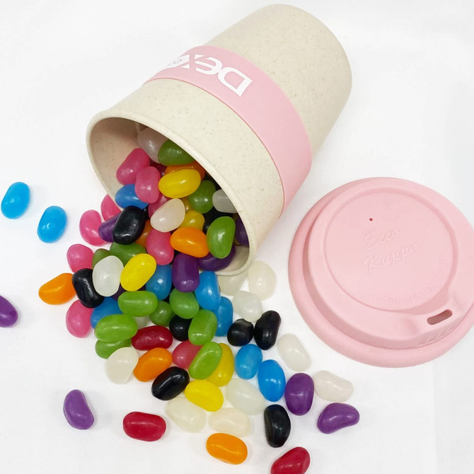 A bamboo cup in pink, spilling an assortment of colourful jelly beans in various shades on a white background.