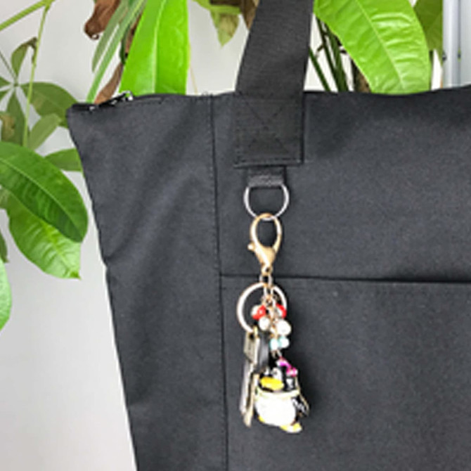 A black nylon tote bag with a loop for keys and a decorative keychain. The bag has a simple, unembellished design.