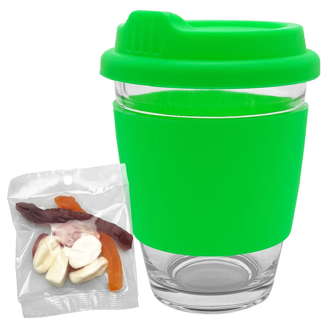 A reusable coffee cup with a bright green silicone lid and sleeve, accompanied by a packet of jelly party mix sweets.