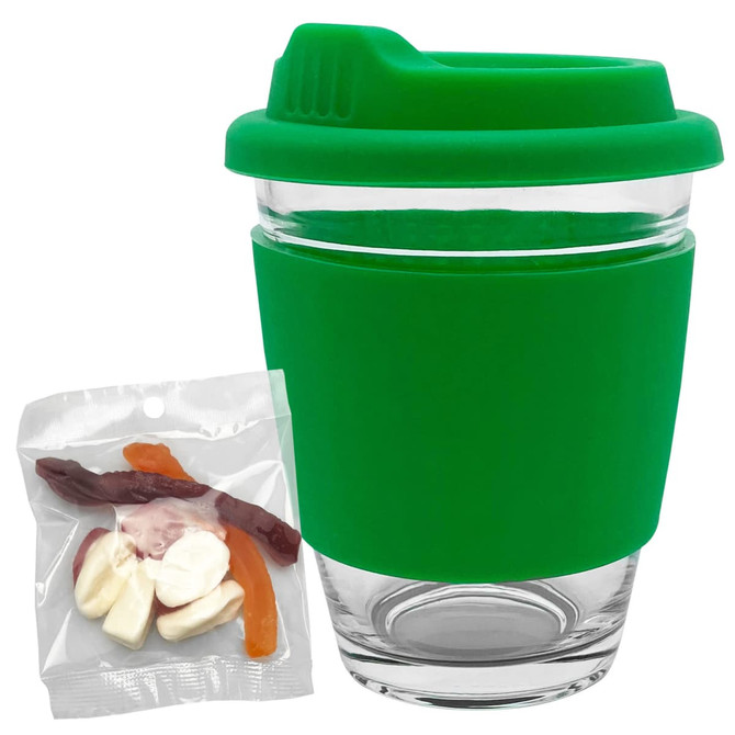A reusable coffee cup with a clear glass body and a green silicone lid and sleeve, accompanied by a pack of jelly lollies.