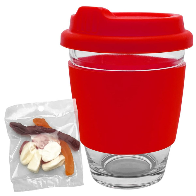 A reusable glass coffee cup with a red silicone sleeve and a red lid, accompanied by a packet of jelly lollies.