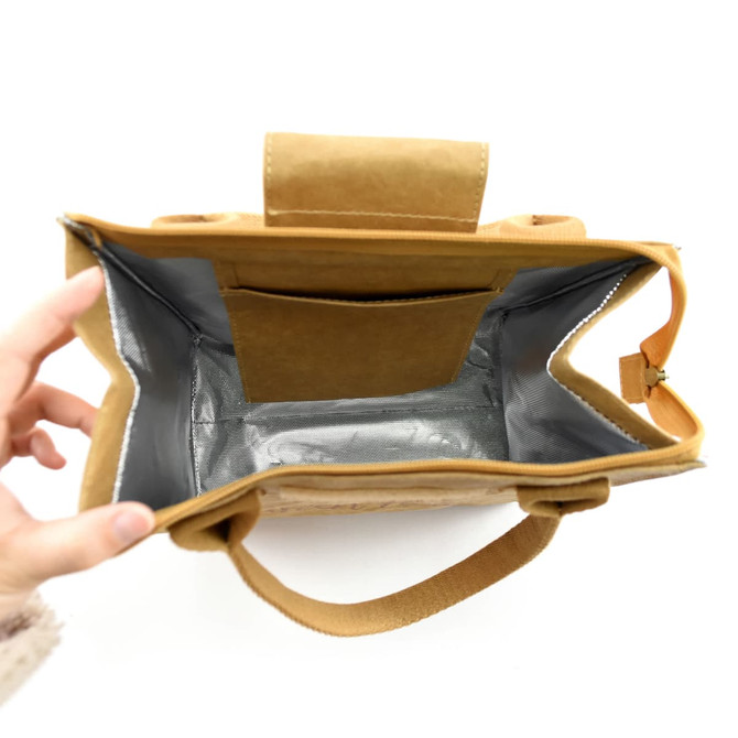 A tan lunch bag with a silver interior and a small pocket, held open by a hand. The bag has padded handles.