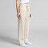 Linen pants in a light beige colour, featuring an elastic waistband and a relaxed fit. The model poses wearing white shoes.
