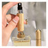 A mini bamboo atomiser held in a hand, with a perfume bottle in the background. The product features a natural bamboo finish.