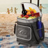 A black cooler trolley with wheels, filled with wine, fruit, snacks, and a blue drink bottle, set on a beach.