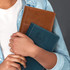 A brown and a teal notebook are held together in a person's arms, showcasing their sleek designs and branding.