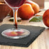 A slate coaster holds a drink beside fresh peaches on a wooden surface, highlighting natural colours and textures.