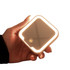 A compact square mirror with an LED light, held in a hand, featuring a soft glow and a neutral colour.