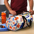 A colourful duffle bag with a vibrant abstract pattern, positioned next to a drink bottle and a towel on a table.