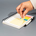 A hand removes a sticky note from a spiral-bound notebook, which features various coloured tabs and a black pen beside it.